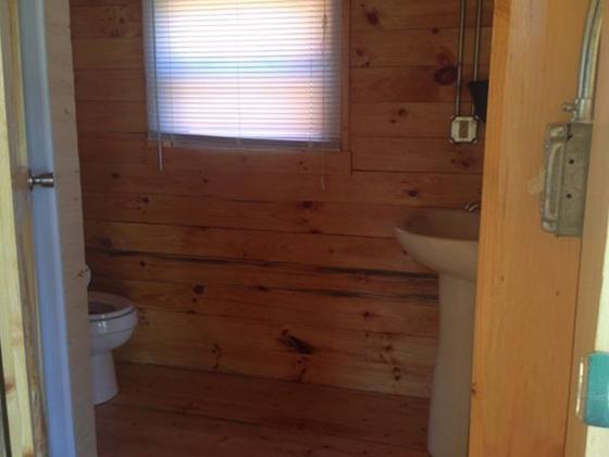 Cabin bathroom with a toilet, pedestal sink, and window with blinds